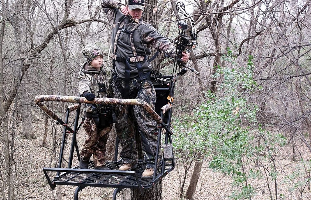 A man and a kid stand on the ladder treestand and hunt