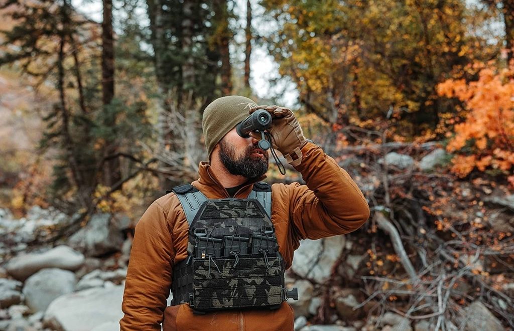 A hunter is standing in the jungle with a thermal scope in his hand
