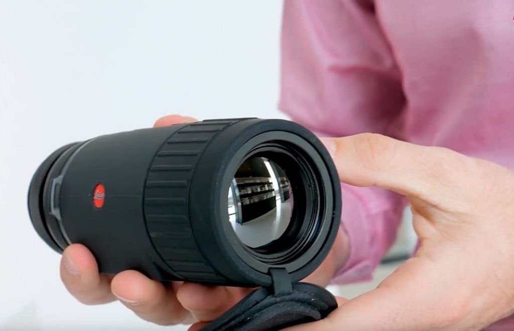 A person is sitting with thermal imaging monocular in hand