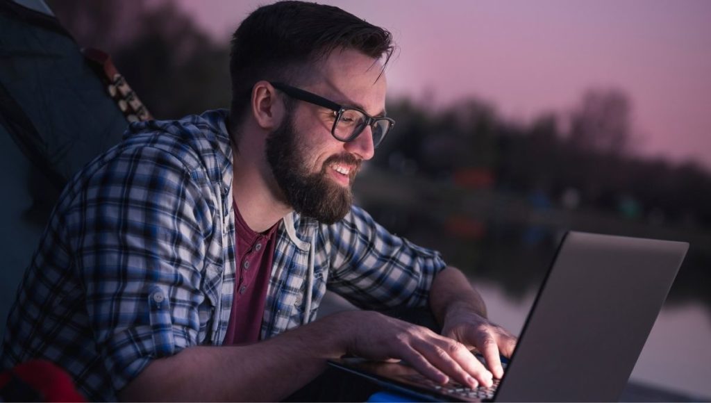 man using laptop in the dark while camping